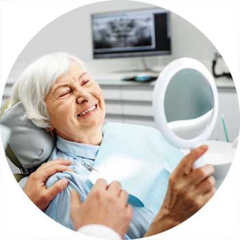Ältere Patientin auf dem Behandlungsstuhl begutachtet ihren neuen Zahnersatz